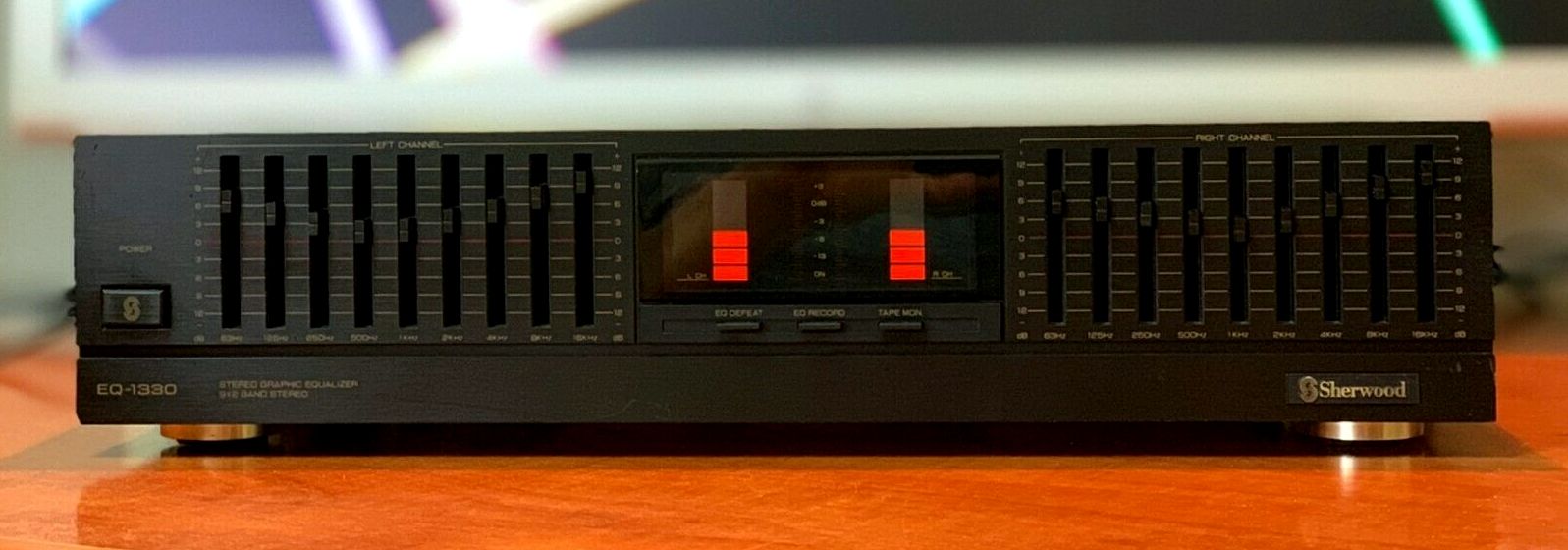 /images/EQ-1330.jpg A stock image of a Sherwood EQ-1330, showing the same positioning of the EQ sliders and VU meters as in the screenshot from The Matrix. It's a black unit, with orange VU meters, the VU meters are segmented into rectangles, and the topmost segment on both left and right VU meters is red instead of orange. There are several EQ band sliders for left and right channels, to the left and right of the VU meters. They are labelled with the various cutoff frequencies between 63Hz and 16Khz.